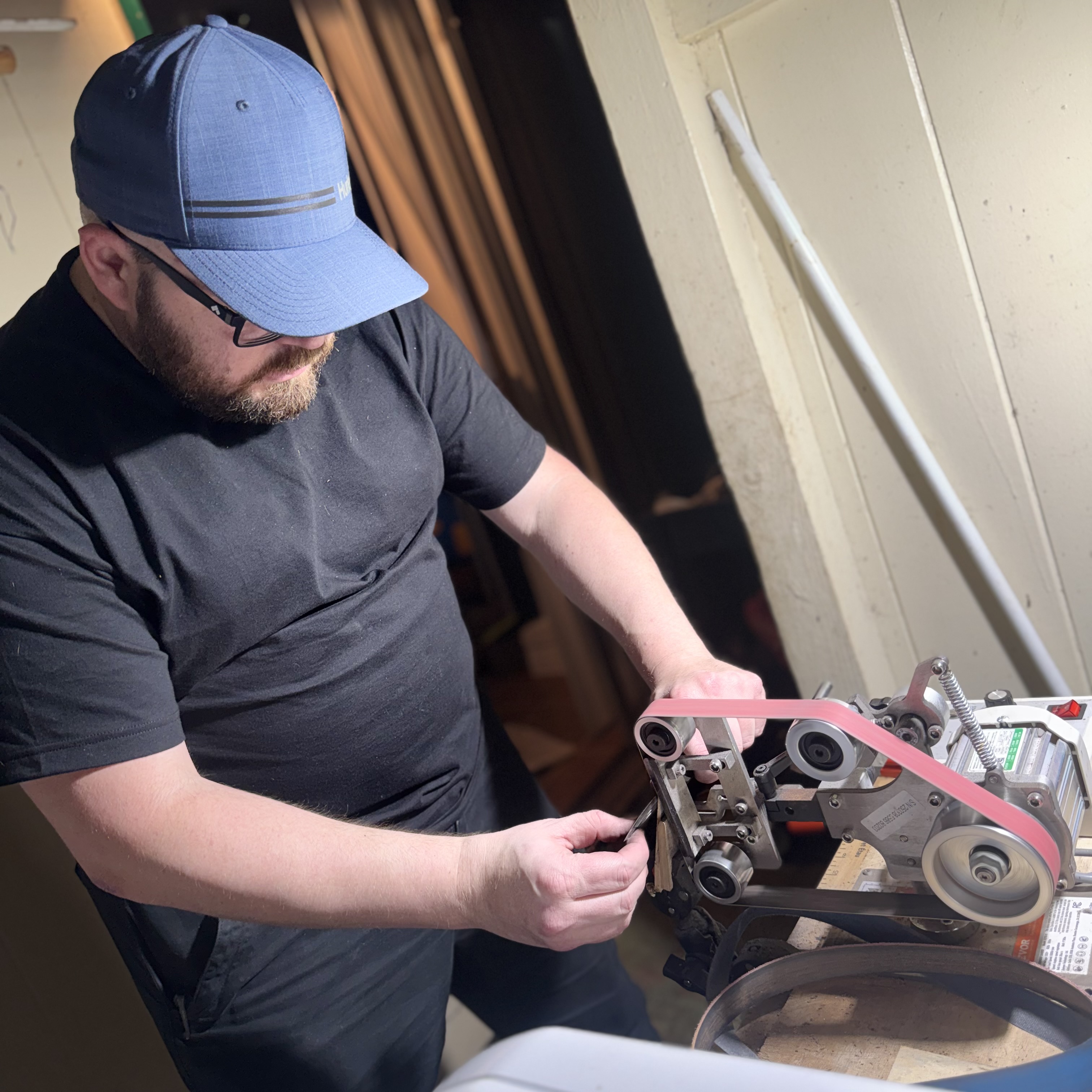 Owner of Sharpening Solutions Hawaii working at a professional belt grinder, sharpening a blade with precision and focus